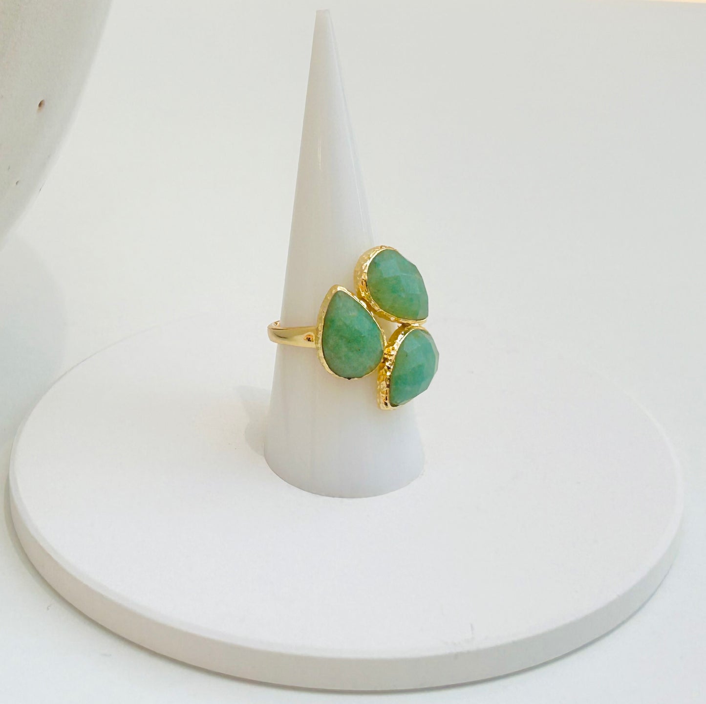 
                  
                    A gold ring with three green Aventurine teardrop-shaped gemstones, displayed on a white cone stand against a white background.
                  
                