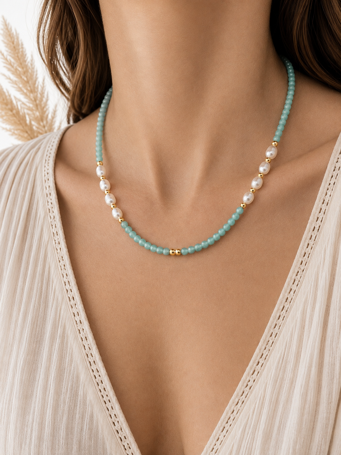 A close-up of a model wearing a delicate necklace featuring light amazonite blue-green beads, white pearls, and small gold spacer beads, styled with a cream-colored lace-trimmed top.