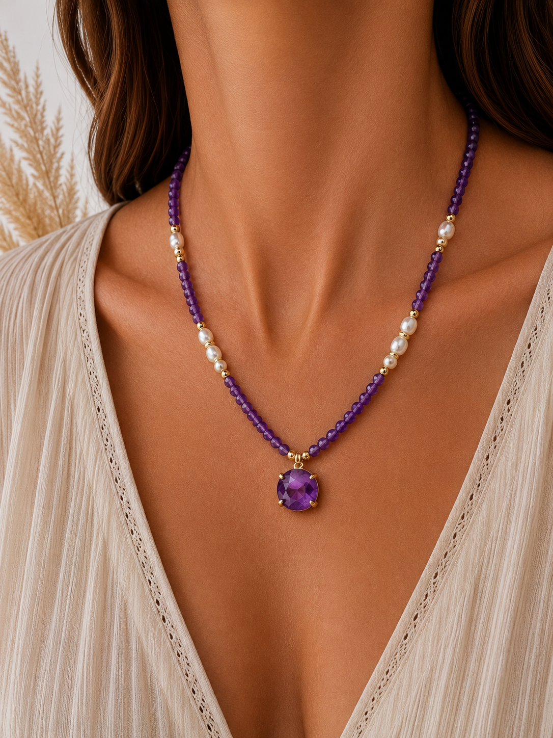 
                  
                    A close-up of a model wearing a beaded necklace with amethyst beads, white pearl-like accents, and a round purple gemstone pendant in gold-toned settings.
                  
                