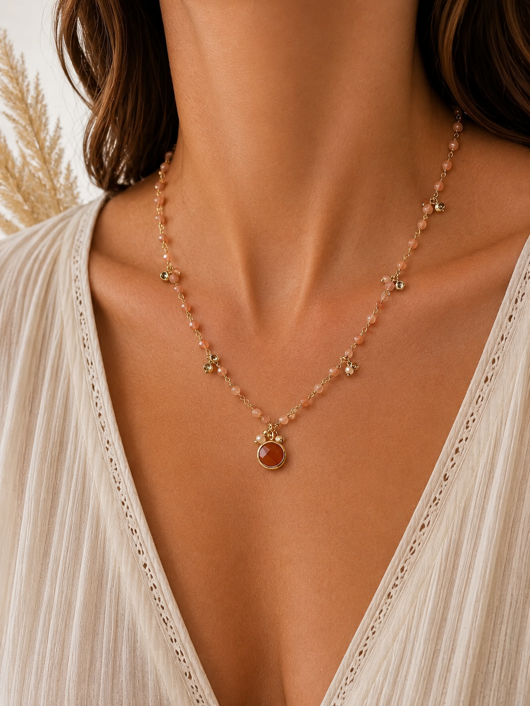 
                  
                    A close-up of a model wearing a delicate gold-toned beaded necklace with a central round sunstone pendant, cubic zirconia pendants paired with a cream-colored lace-trim V-neck top.
                  
                