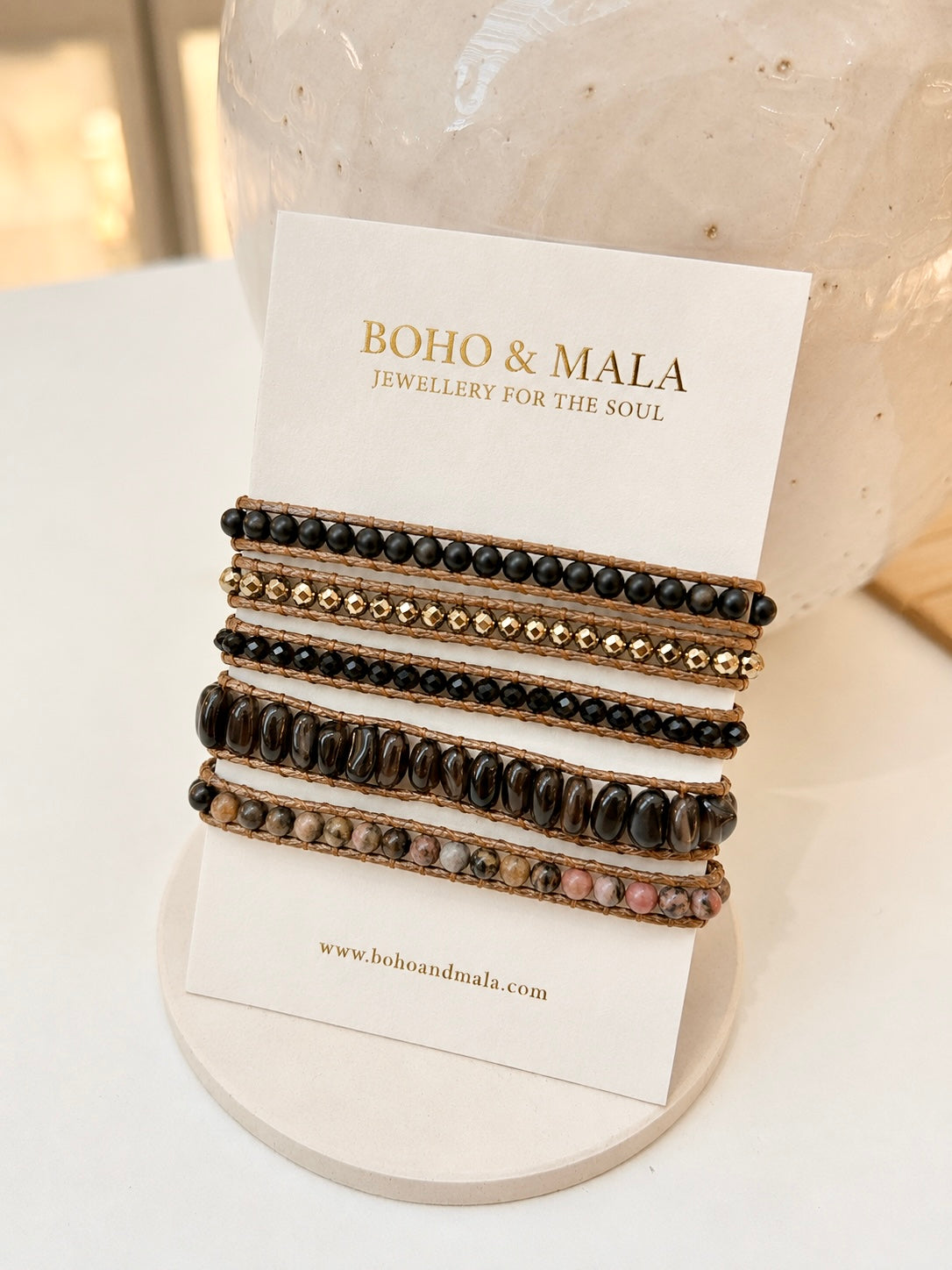 Four beaded natural stone wrap bracelets displayed on a white card branded BOHO & MALA, set against a soft-focus white and beige background.