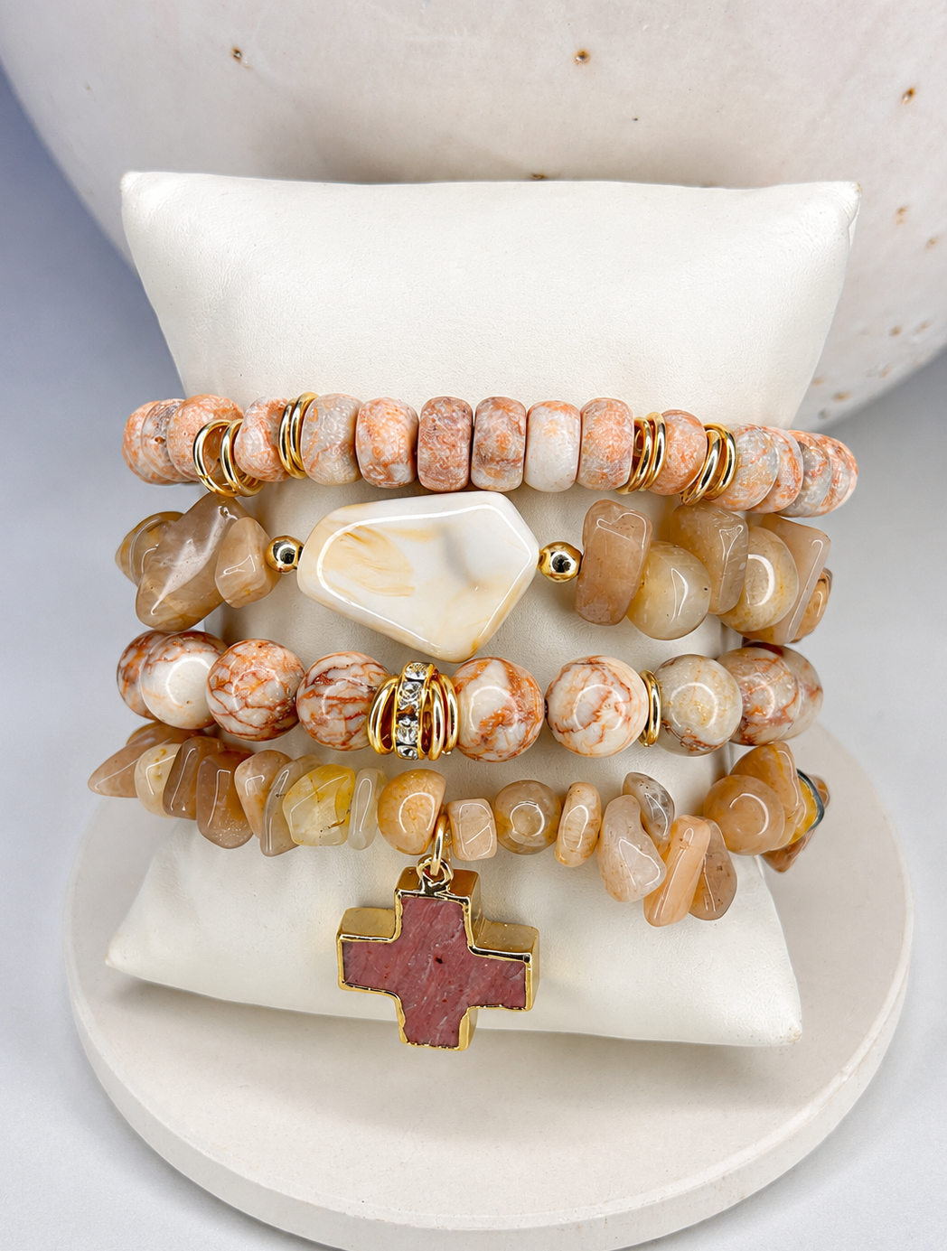 Stack of pink marbled gemstone and gold bracelet set on a marble surface