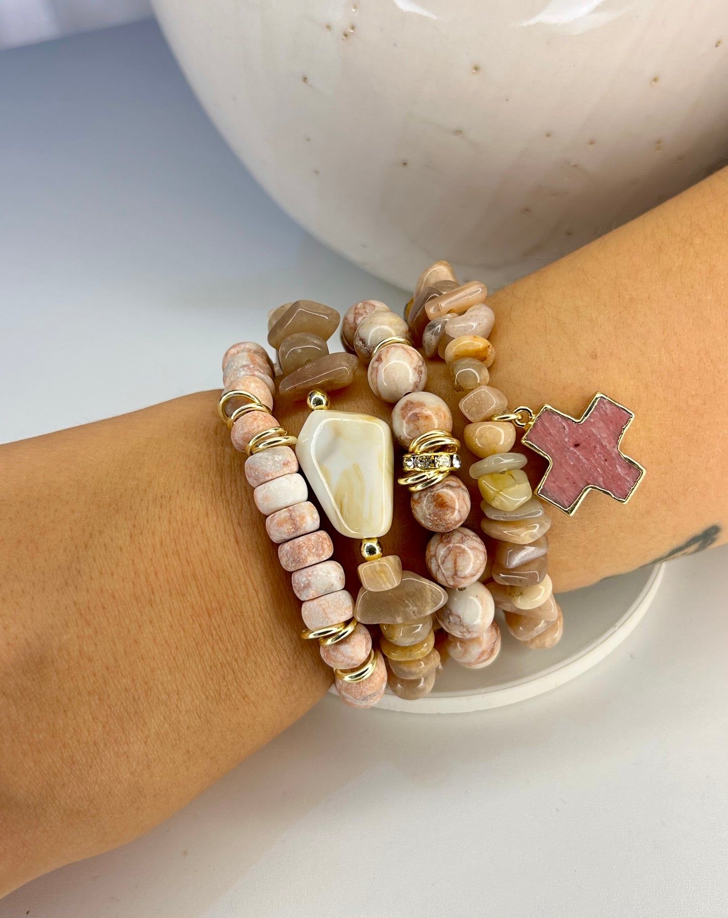 Stack of beaded pink marbled gemstone bracelets on a wrist with a neutral background