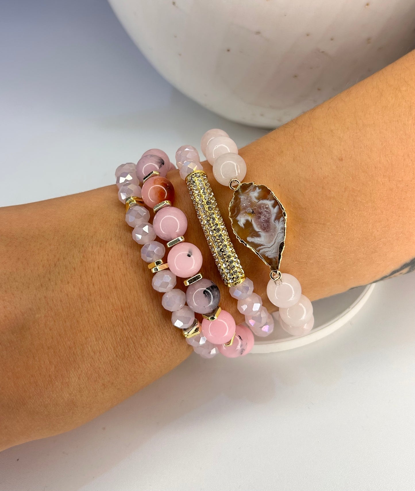 Stack of pink mixed rose quartz  beaded bracelets on a wrist with a neutral background