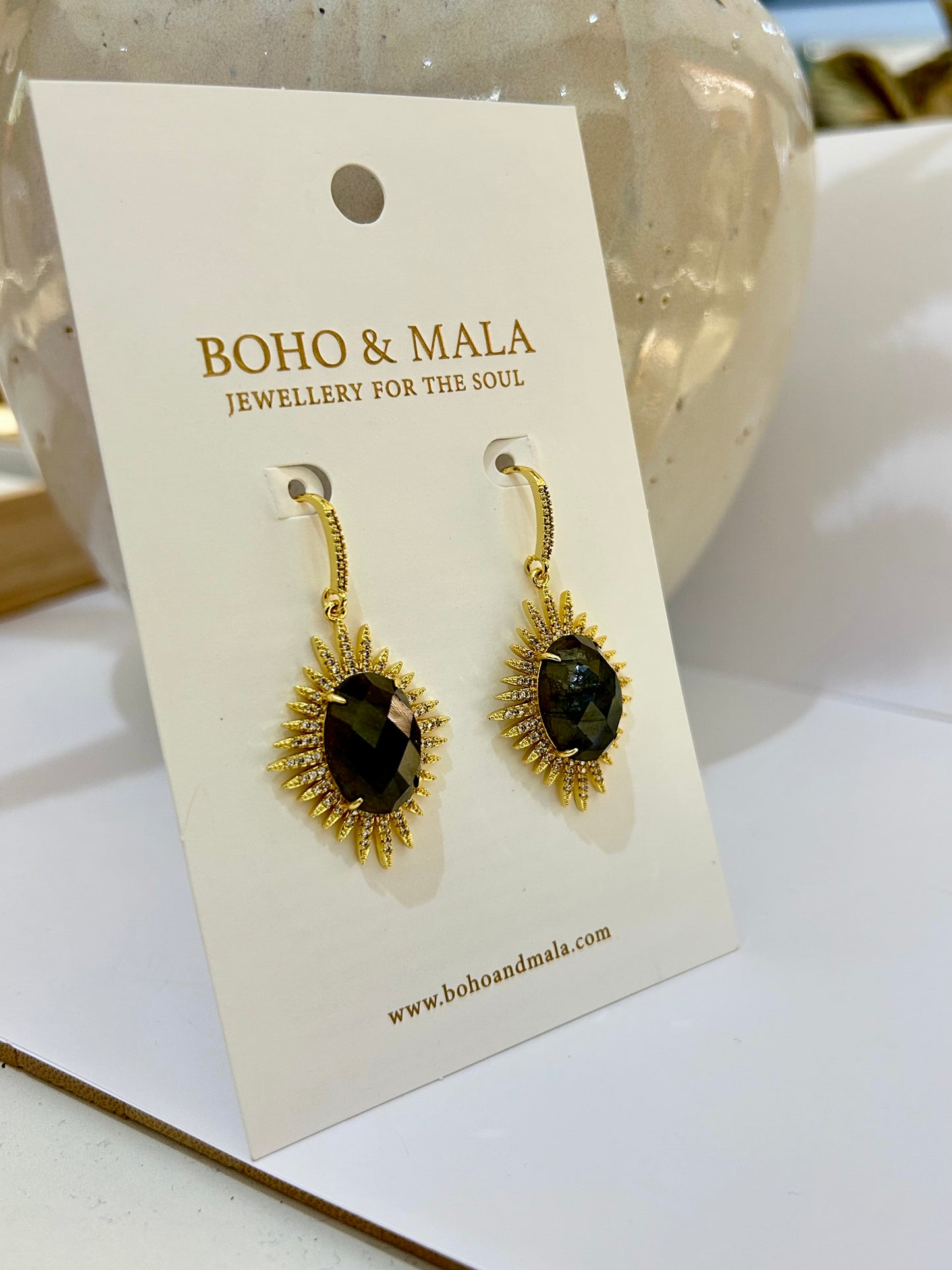 
                  
                    Gold earrings with green stones on a BOHO & MALA branded card.
                  
                