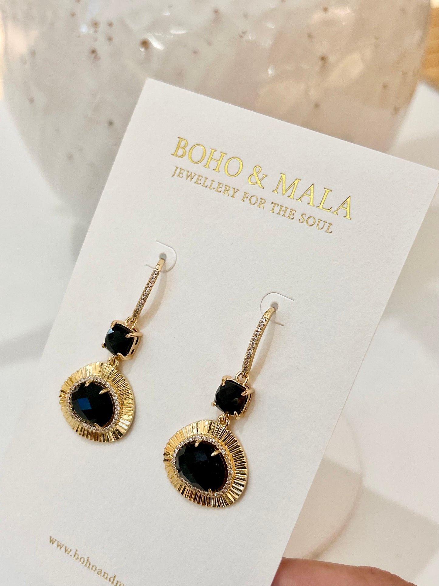 
                  
                    Gold earrings with black obsidian stones on a 'Boho & Mala' branded card.
                  
                