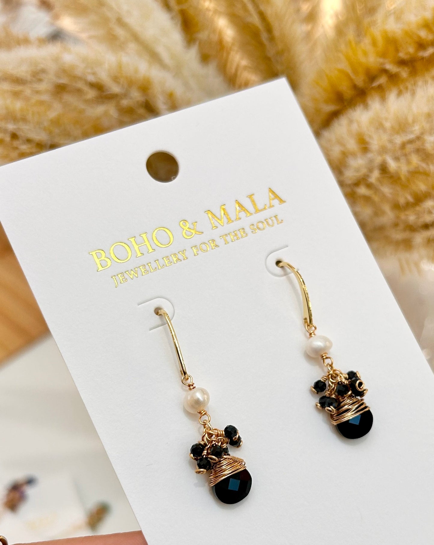 
                  
                    Pair of earrings on a BOHO & BALA branded card held by a hand 
                  
                