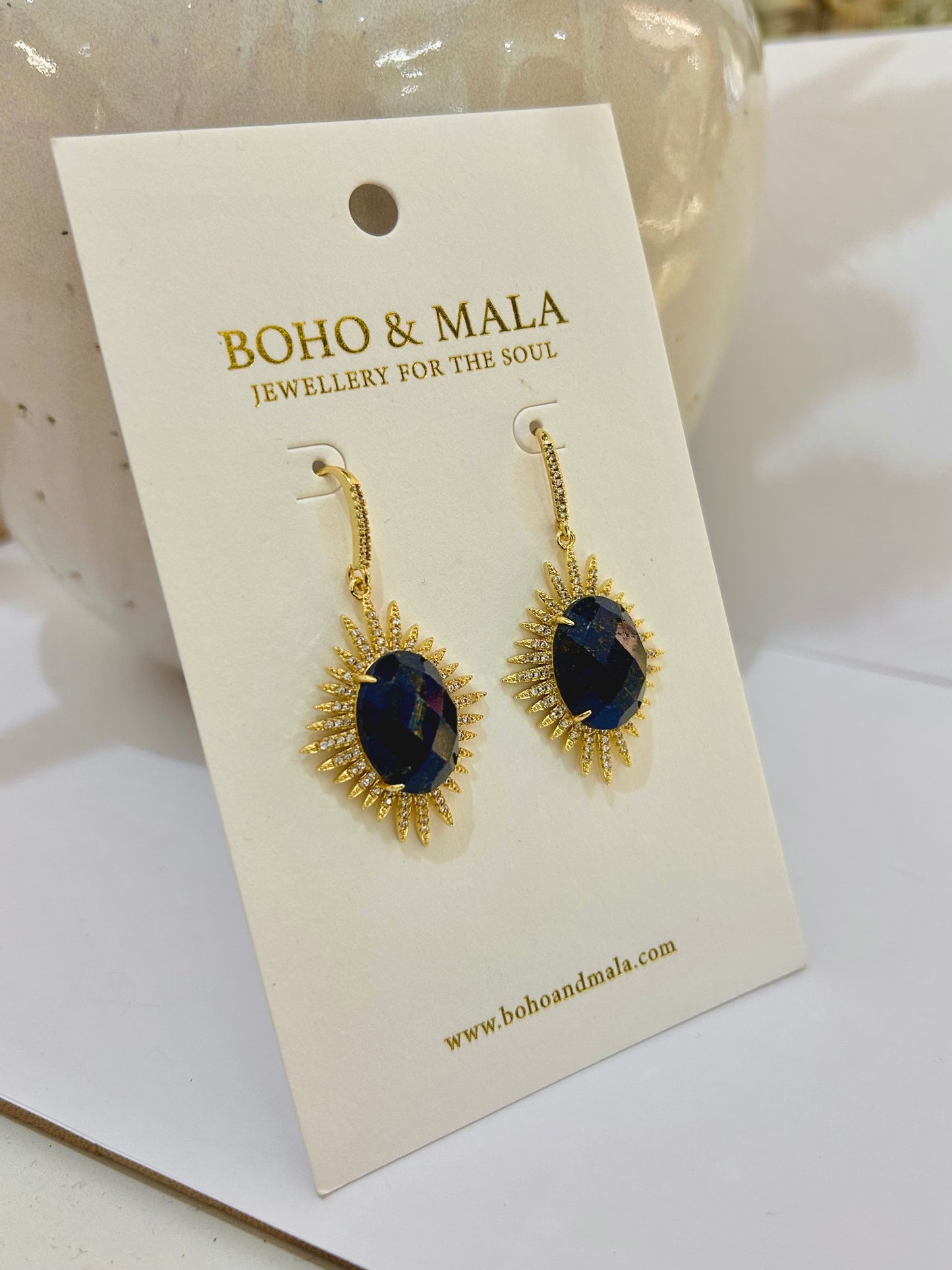 
                  
                    Gold earrings with blue lapis stones on a BOHO & MALA branded card.
                  
                