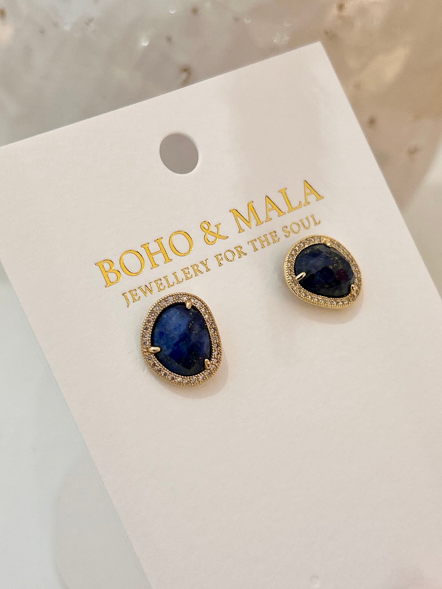 
                  
                    Gold earrings with dark gemstones on a 'Boho & Malia' branded card.
                  
                