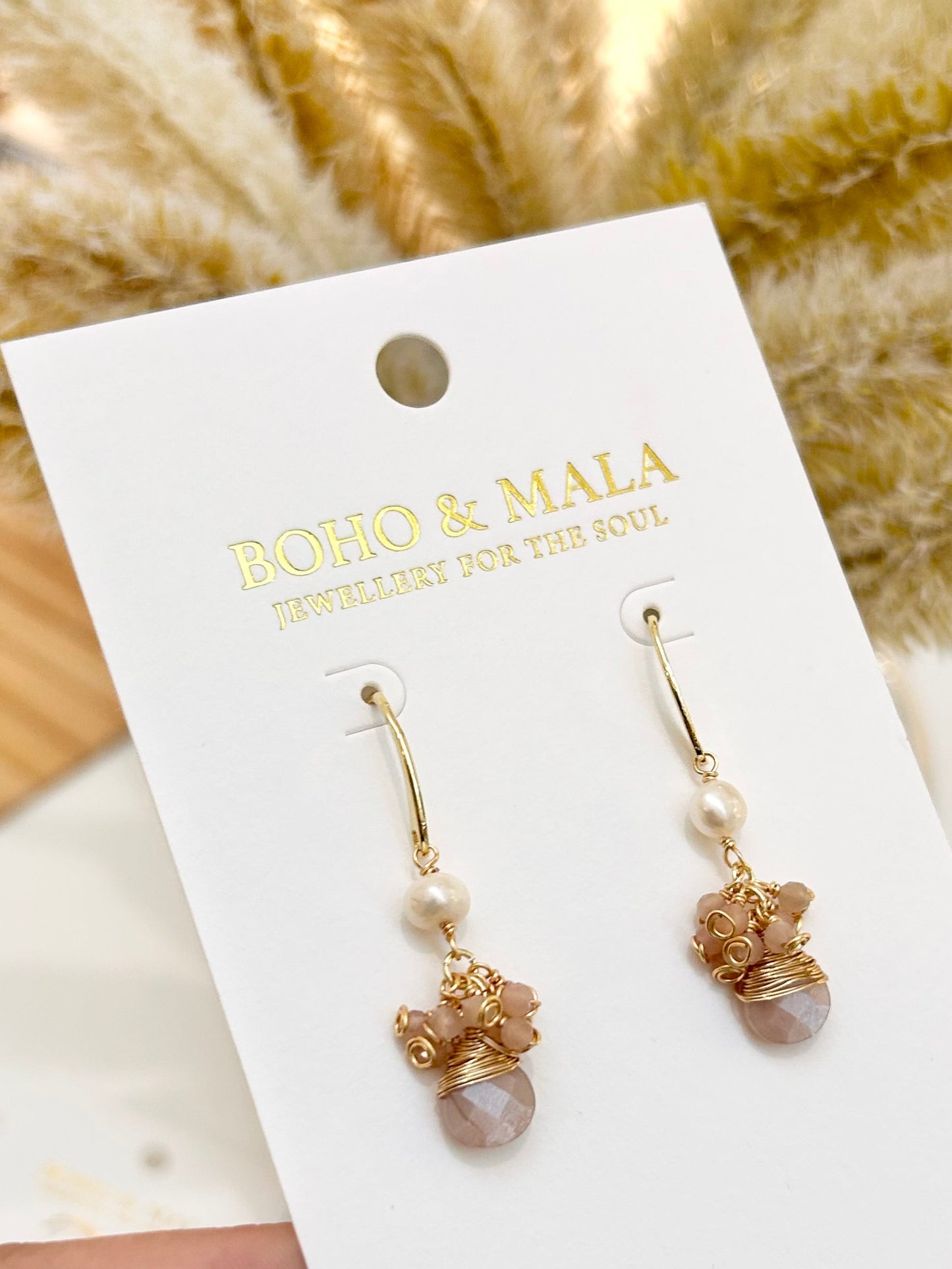 
                  
                    Gold and pearl earrings on a BOHO & MALA branded card with a blurred natural background
                  
                