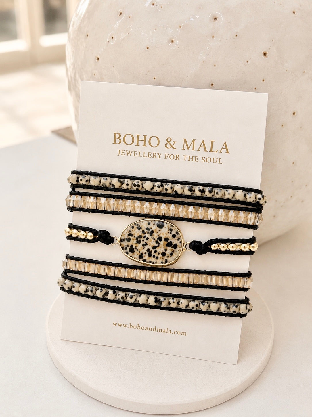Handcrafted multi-wrap bracelet featuring natural Dalmatian Jasper beads, gold-toned accent beads and a central Dalmatian Jasper stone on black leather cord, displayed on a Boho & Mala jewellery card.