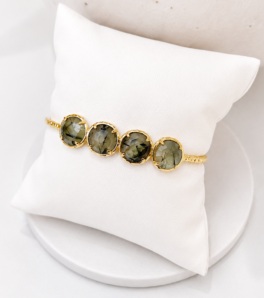 
                  
                    Bracelet with prehnite gemstones on a white stand against a neutral background
                  
                