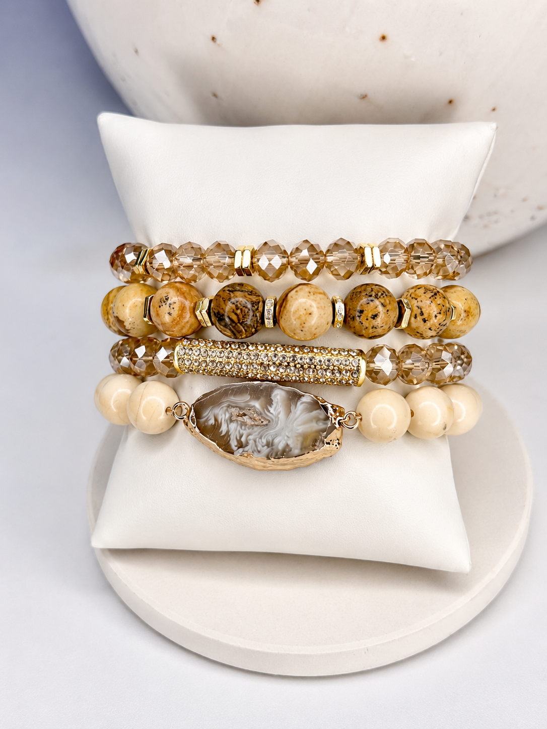 Set of beaded desert jasper bracelets on a white ceramic holder with a textured background