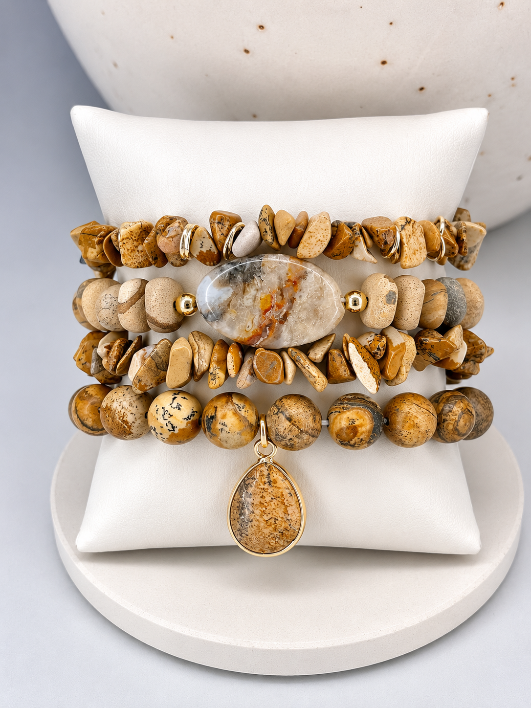 Stack of beaded desert jasper stone on a stacked bracelets with a central stone and pendant on a white surface.