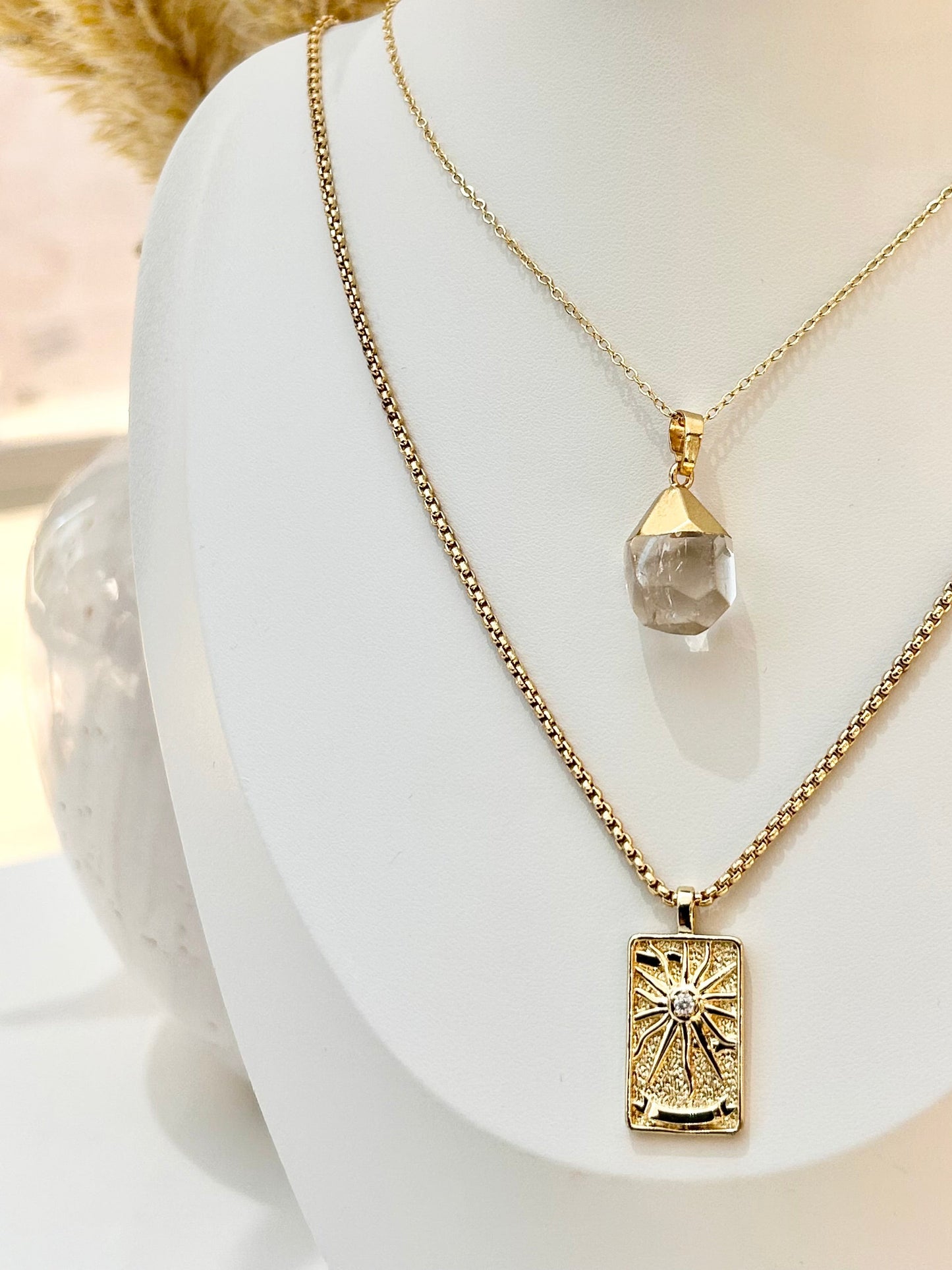 
                  
                    Two gold necklaces with pendants on a mannequin bust.
                  
                