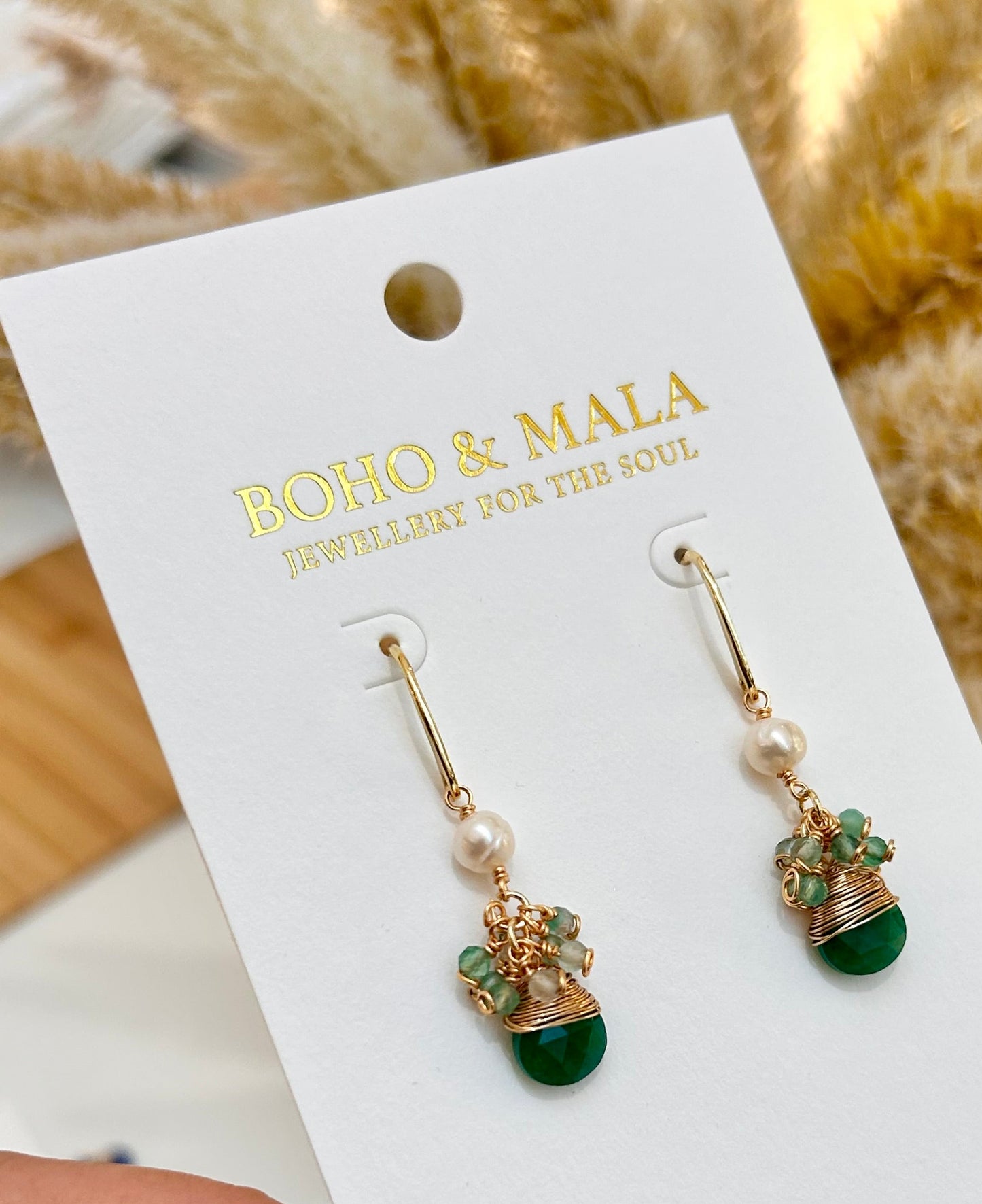 
                  
                    Pair of earrings on a 'Boho & Malia' branded card held by a hand.
                  
                