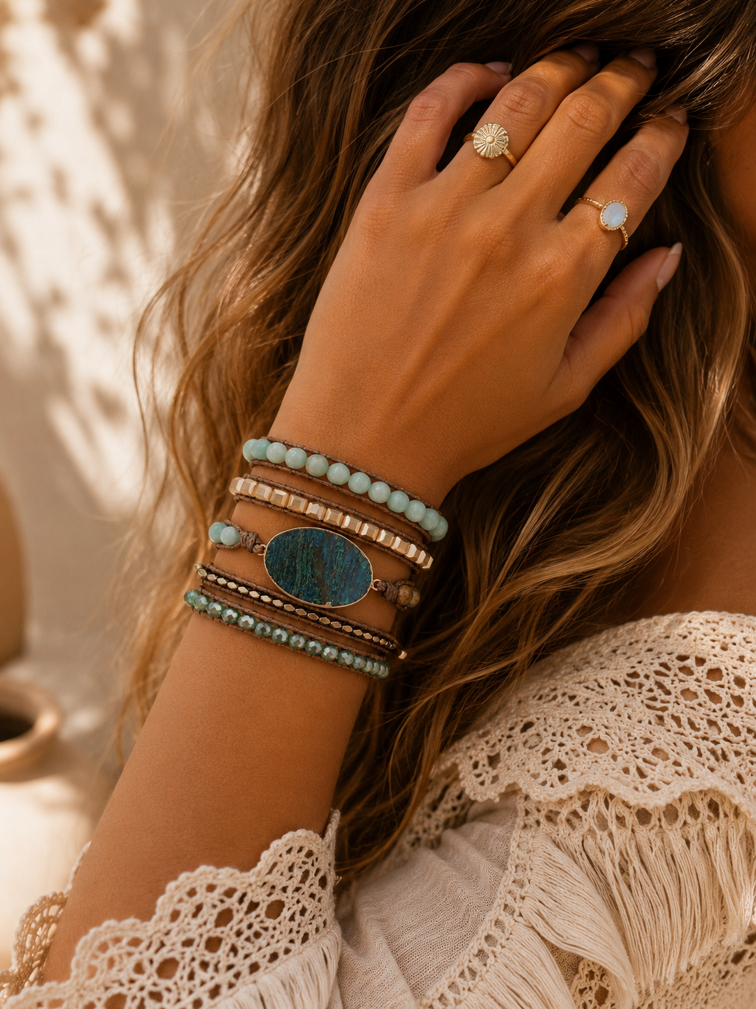 
                  
                    Close-up of a hand wearing chrysocolla wrap bracelets and rings with a textured background
                  
                
