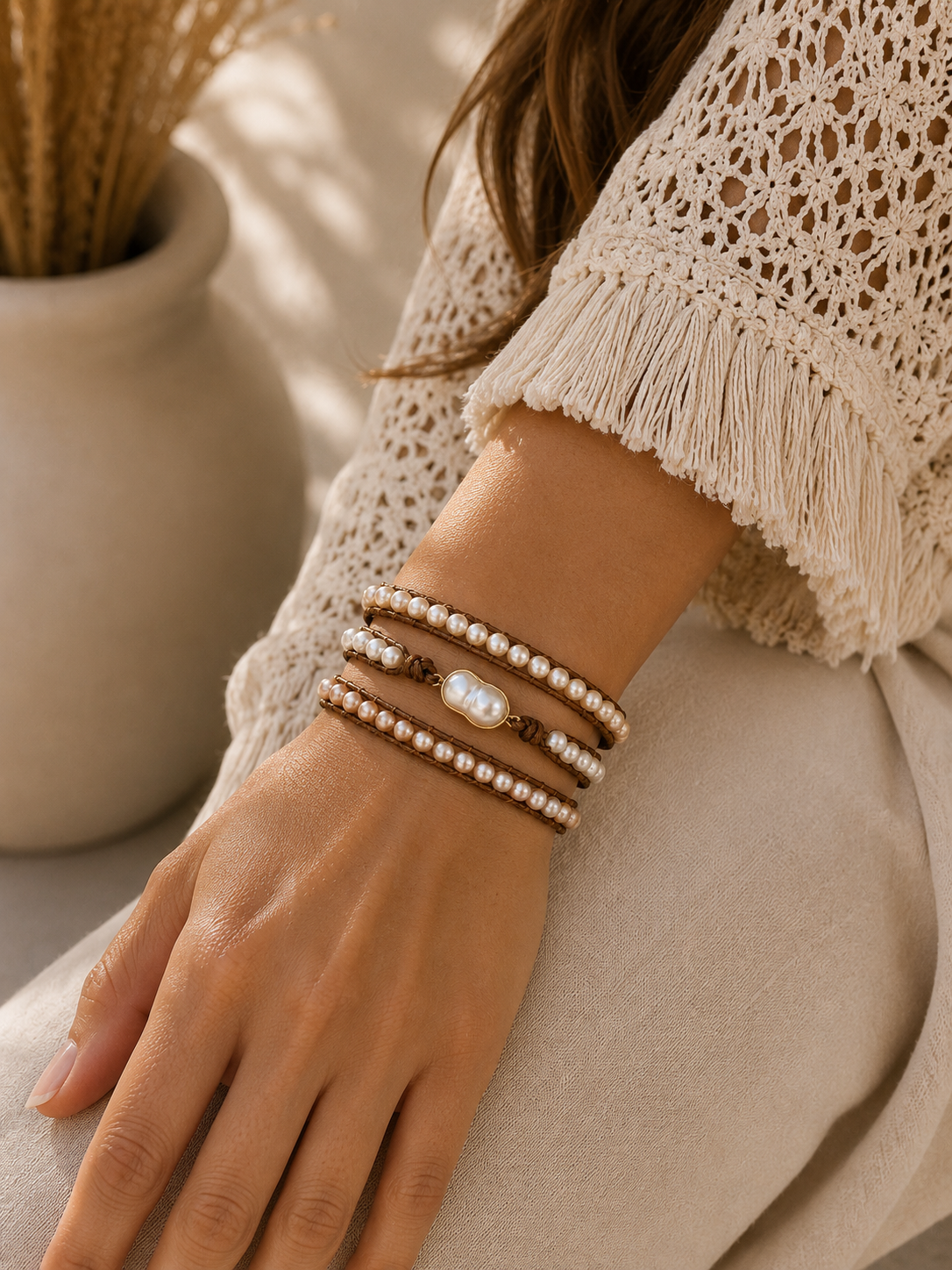 
                  
                    Close-up of a hand wearing wrap pearl bracelets with a neutral background
                  
                