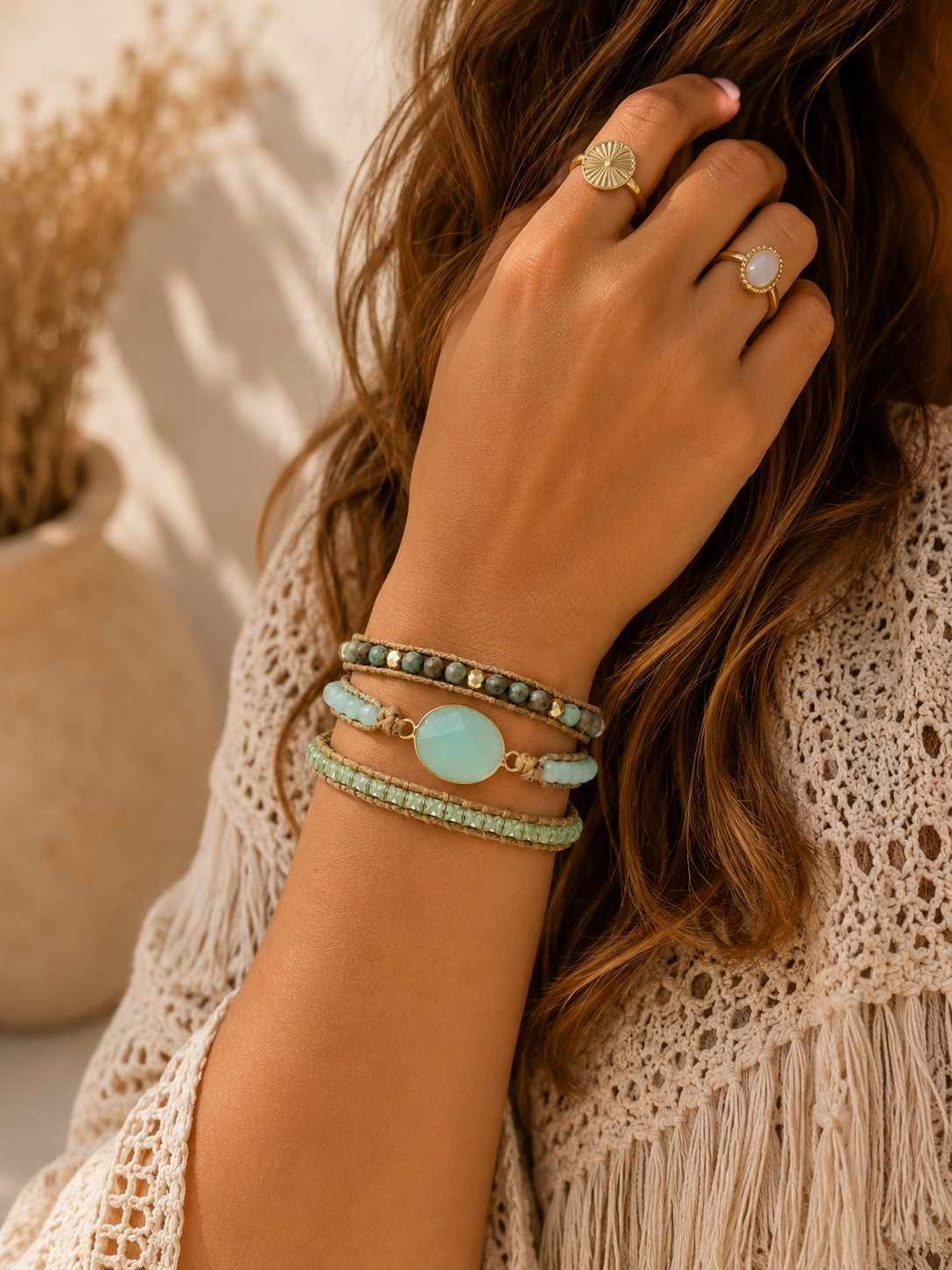
                  
                    Hand wearing green mixed stone wrap bracelets and rings with a textured background
                  
                