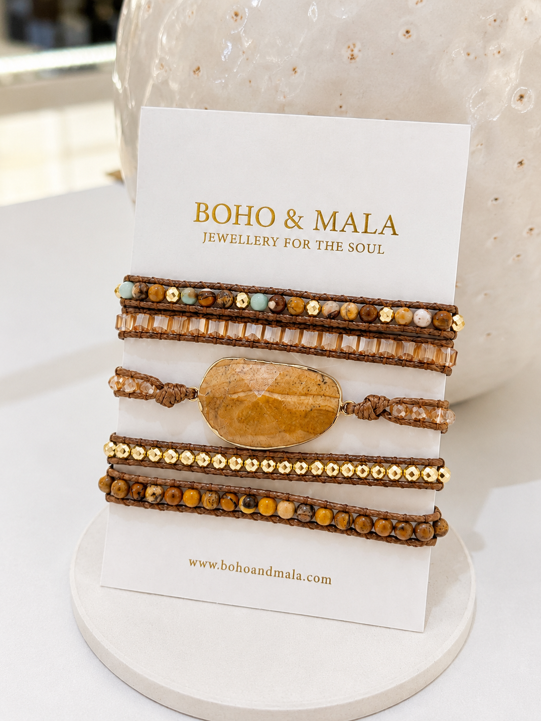 Four bohemian-style beaded bracelets from Boho & Mala, featuring brown cords, gold and beige beads, and a central picture jasper stone, displayed on a white branded card.