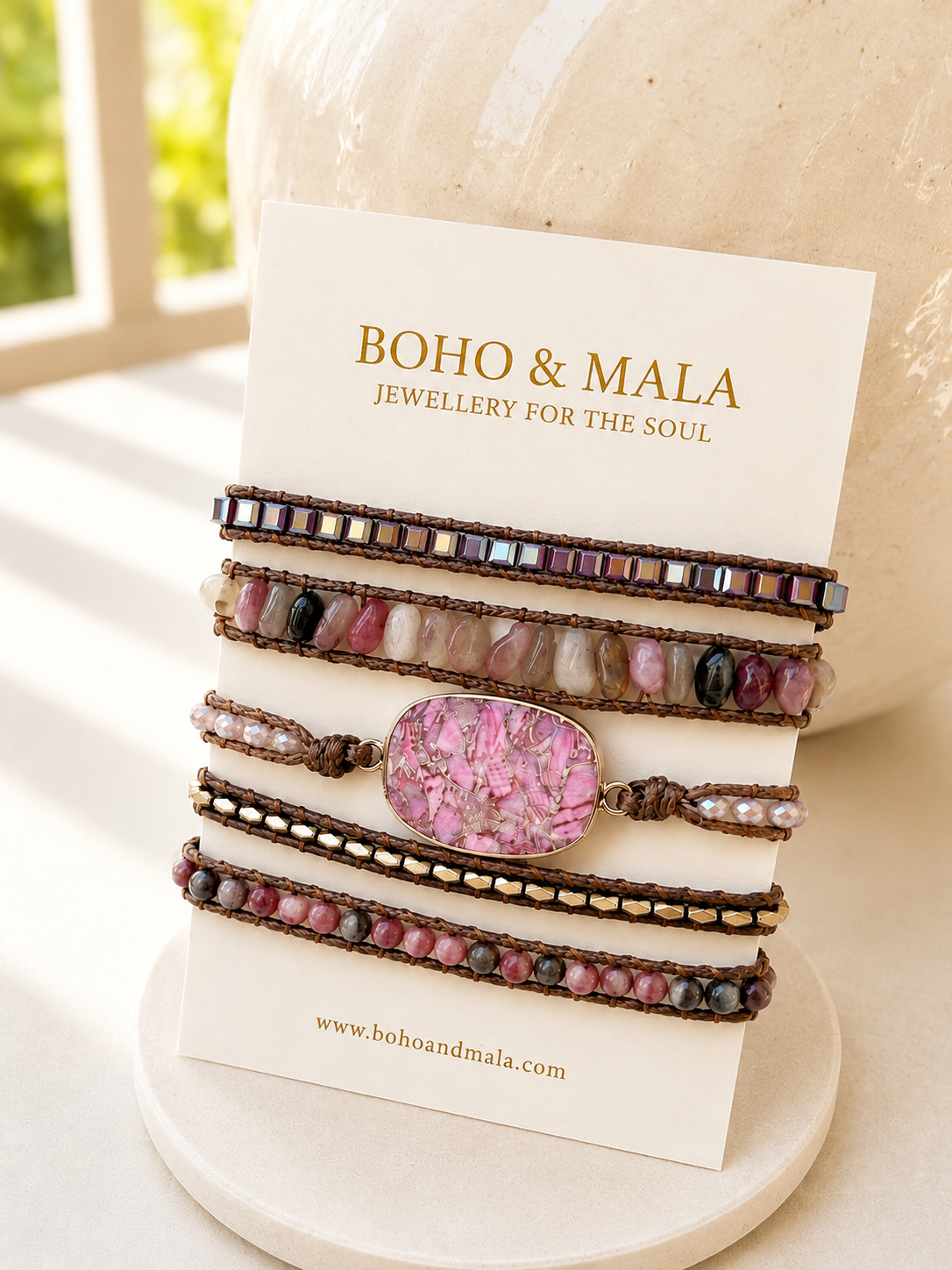 Set of Boho & Mala wrap bracelets with rhodonite stone on a white stand with a blurred background