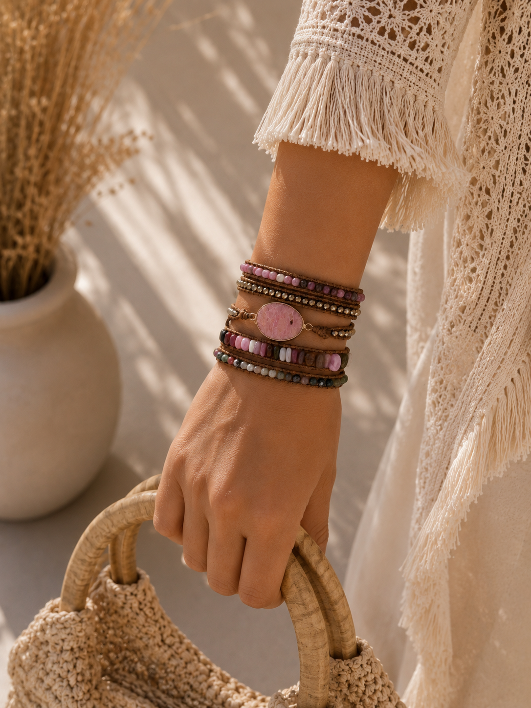 
                  
                    Hand wearing rhodonite mixed wrap bracelets holding a woven bag with a neutral background
                  
                