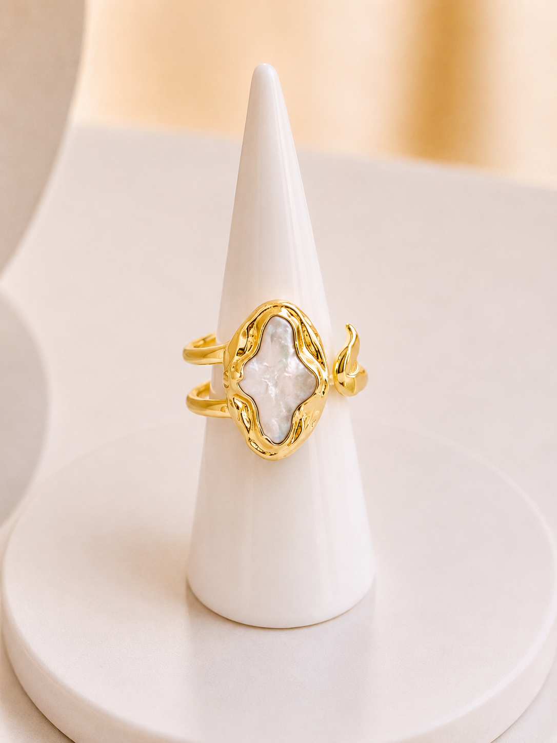 A gold ring with a textured, organic-shaped bezel holding a freshwater pearl marquise-cut gemstone, displayed on a white cone jewellery stand.