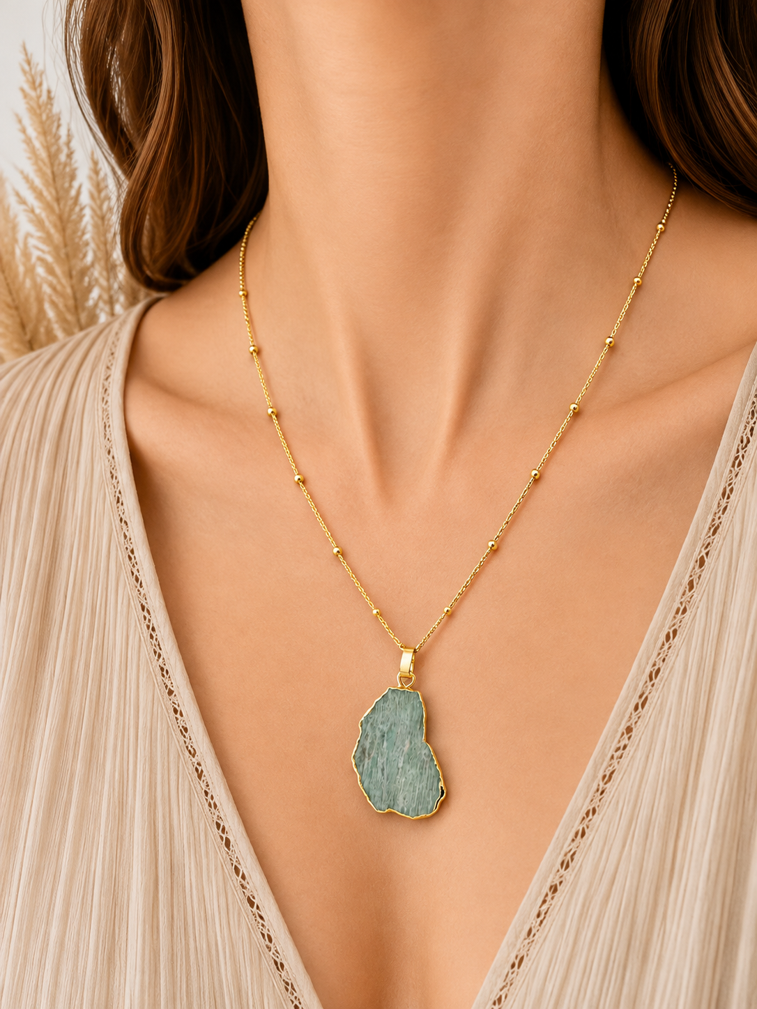 A close-up of a model wearing a delicate gold chain necklace with a raw, irregular-shaped amazonite stone pendant.