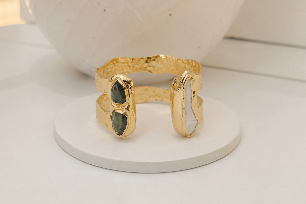 Gold-plated double-band open cuff bracelet featuring two labradroite stones and a long freshwater pearl in organic settings, displayed on a white jewellery stand.