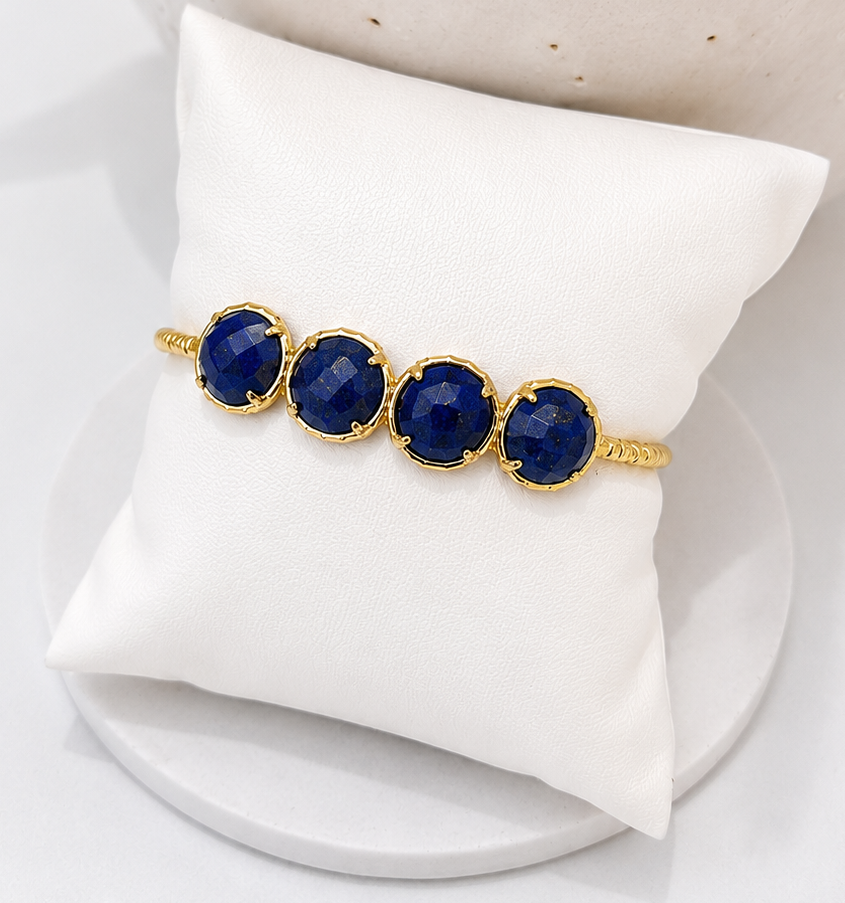 
                  
                    Gold bracelet with Lapis Lazuli on a white cushion against a beige background
                  
                