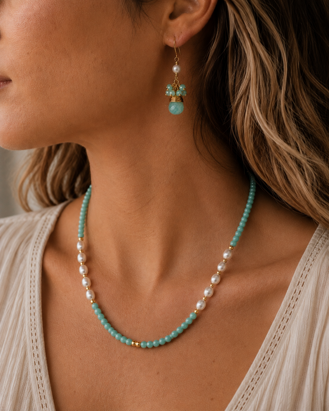
                  
                    A close-up lifestyle shot of a woman wearing a matching amazonite and pearl beaded necklace and dangle earring with gold-toned metal details.
                  
                