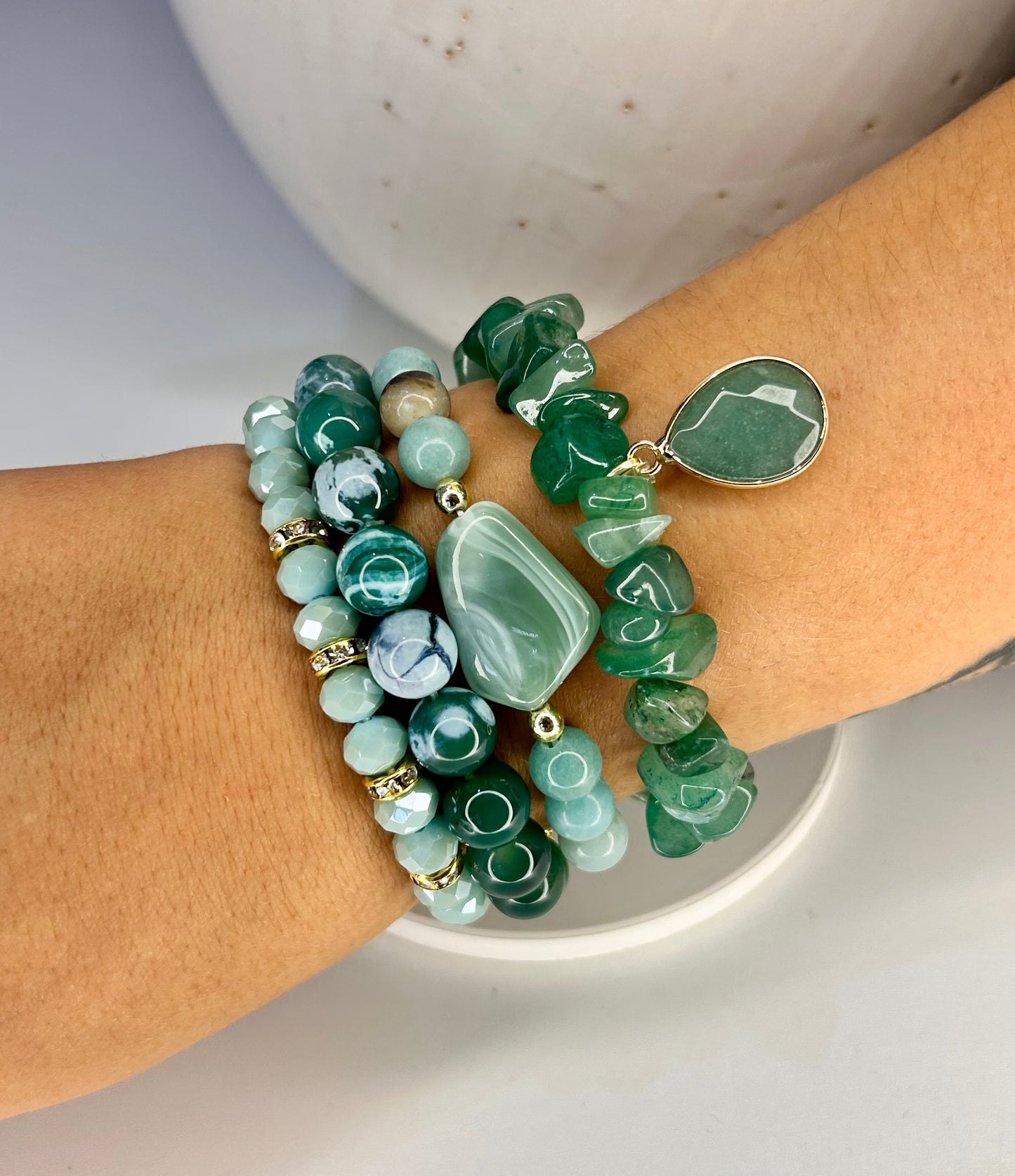 Stack of green natural beaded bracelets on a wrist with a neutral background