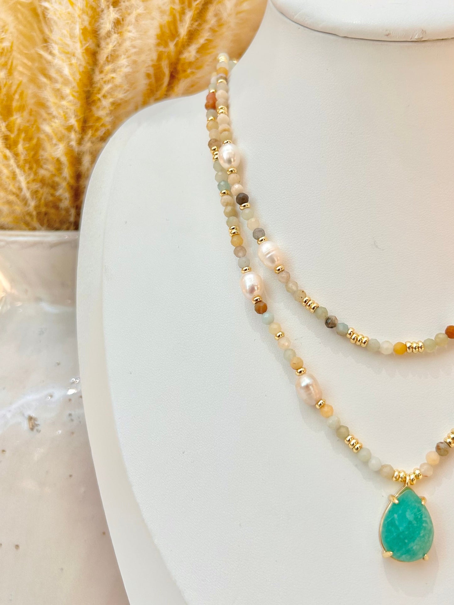 A double-strand beaded necklace with a teardrop-shaped amazonite pendant, displayed on a white jewellery bust. The necklace features white pearls, mixed amazonite stones of light green and gray beads, and small gold spacer beads.