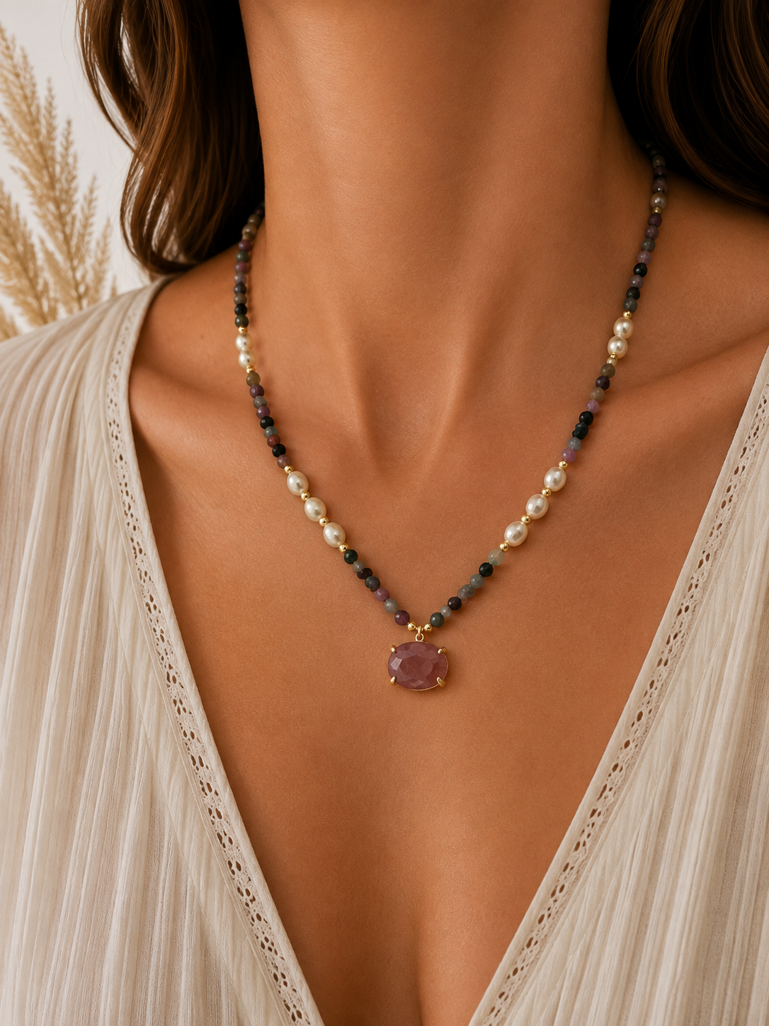 
                  
                    A close-up of a woman wearing a delicate mixed straweberry quartz beaded necklace with a lavender-purple pendant, styled with a cream-colored lace-trimmed top.
                  
                