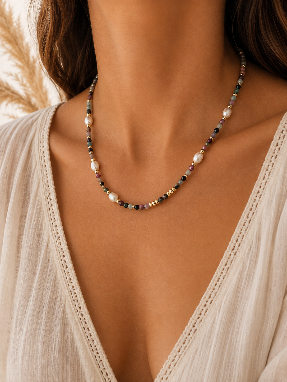 A close-up of a woman wearing a delicate beaded necklace with white pearls and small mixed sunstone beads, paired with a cream lace-trim V-neck top.