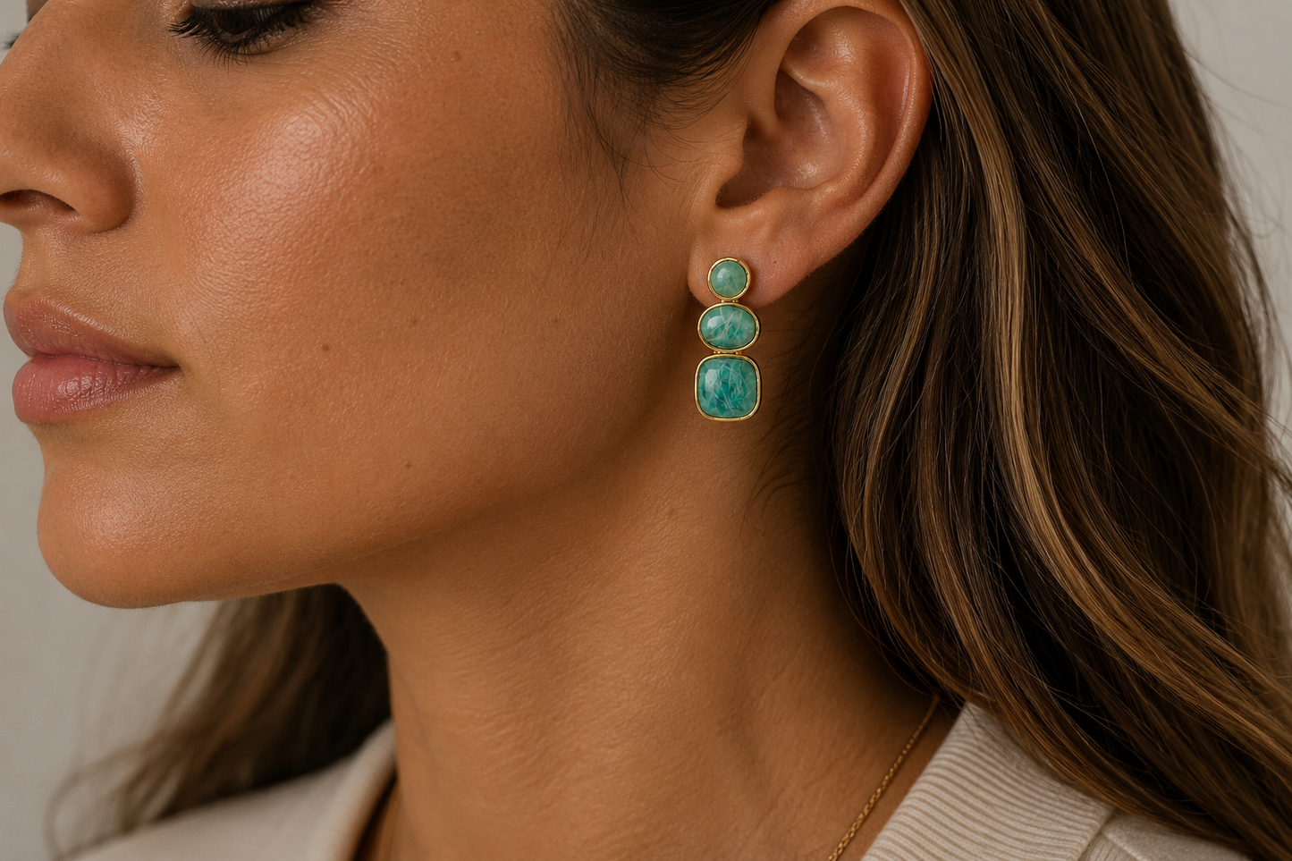 A close-up side profile of a woman wearing a gold drop earring with three stacked oval Amazonite stones.