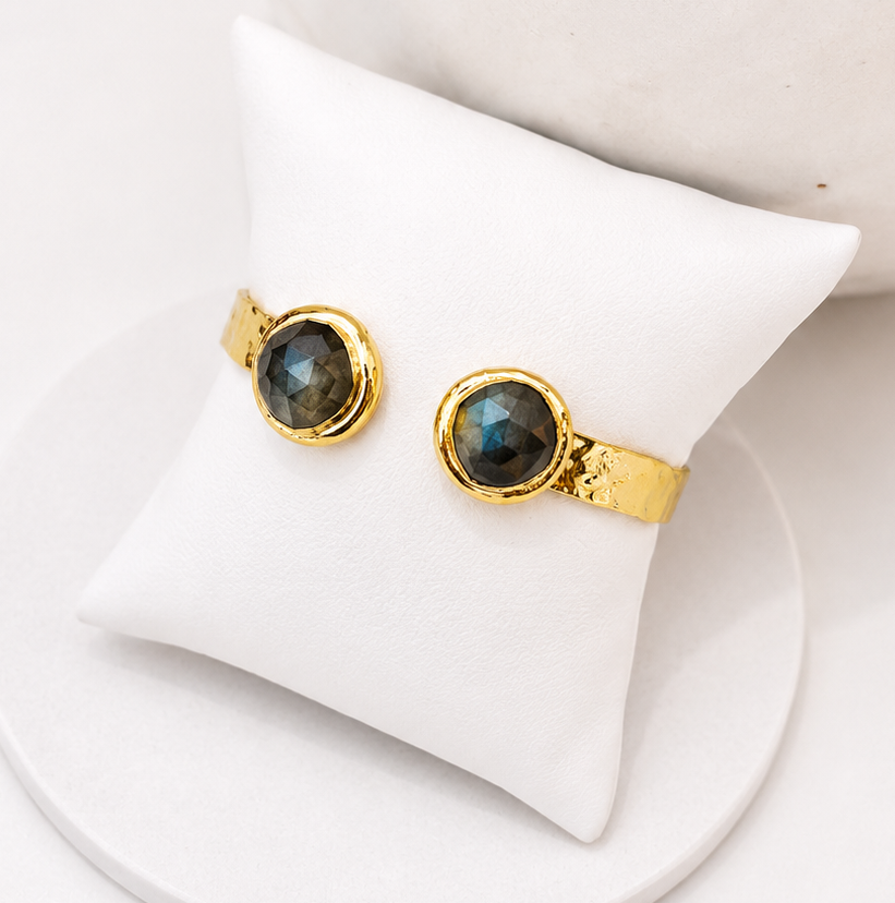 
                  
                    Gold open cuff hammered bangle with labradorite natural gemstones on a white pillow display stand 
                  
                