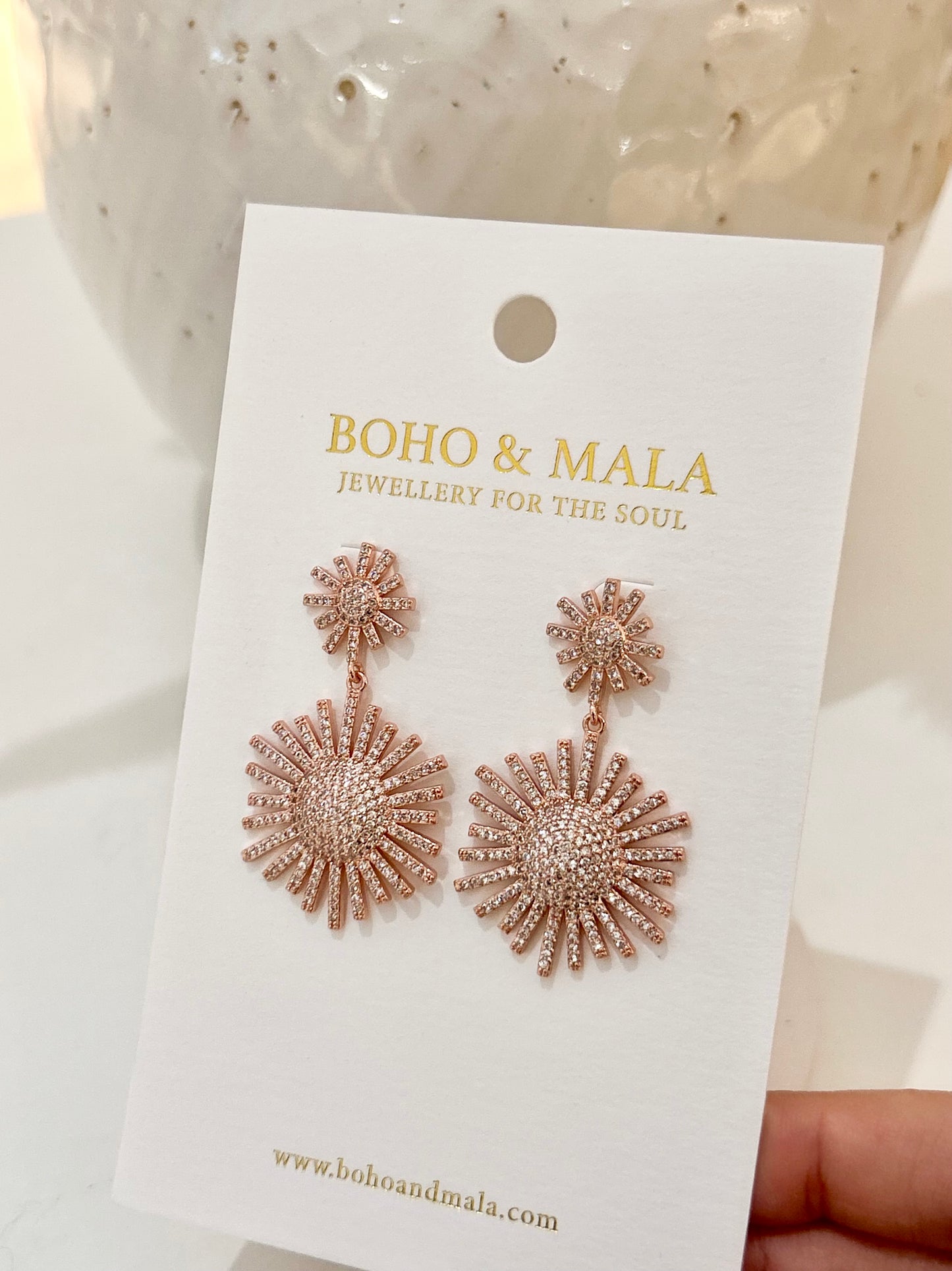 
                  
                    Rose gold earrings on a 'Boho & Mala' branded card with a blurred background
                  
                