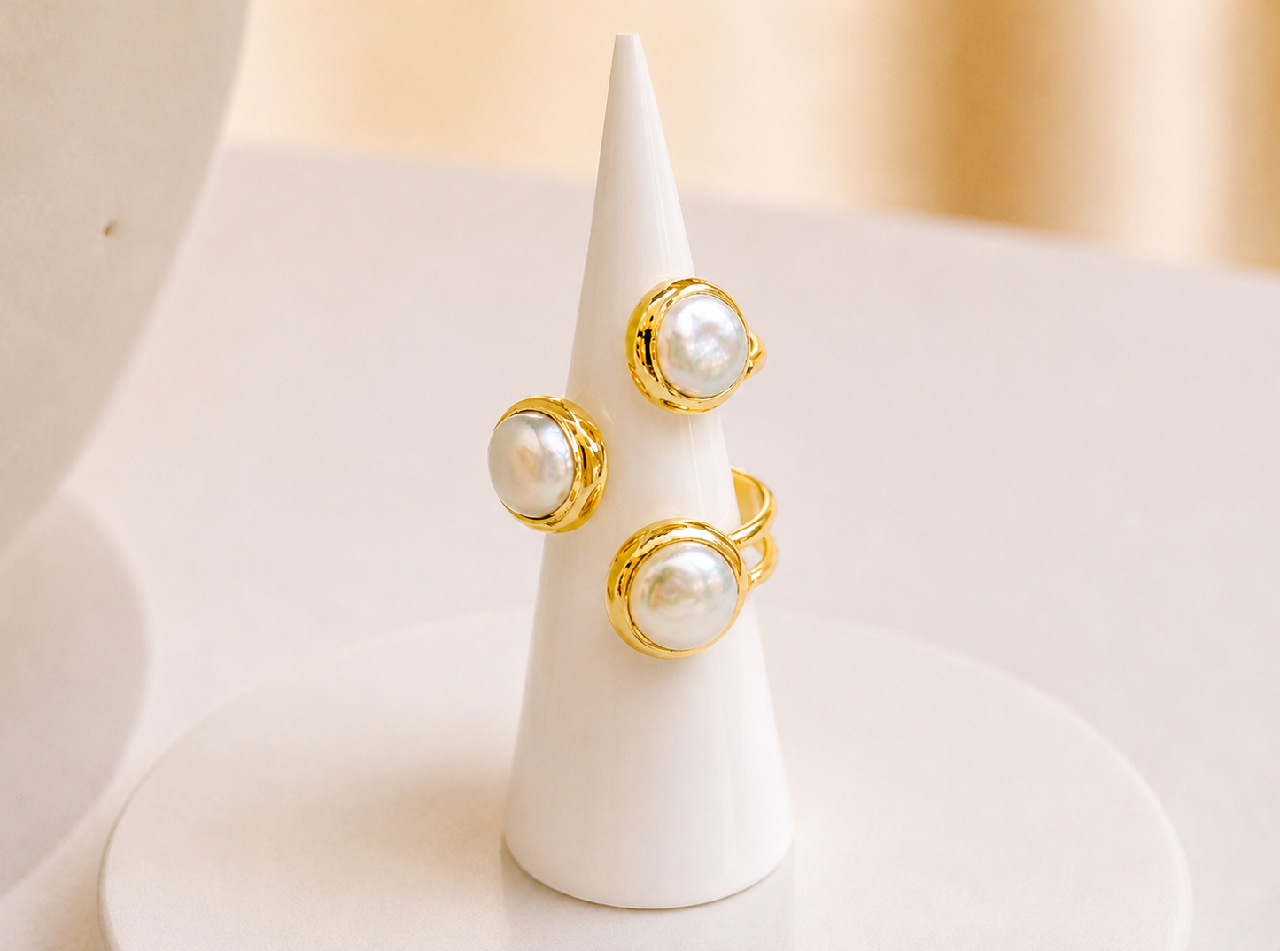 Three gold fresh water pearl stones on an adjustable ring,  displayed on a white cone jewellery stand against a soft beige background.