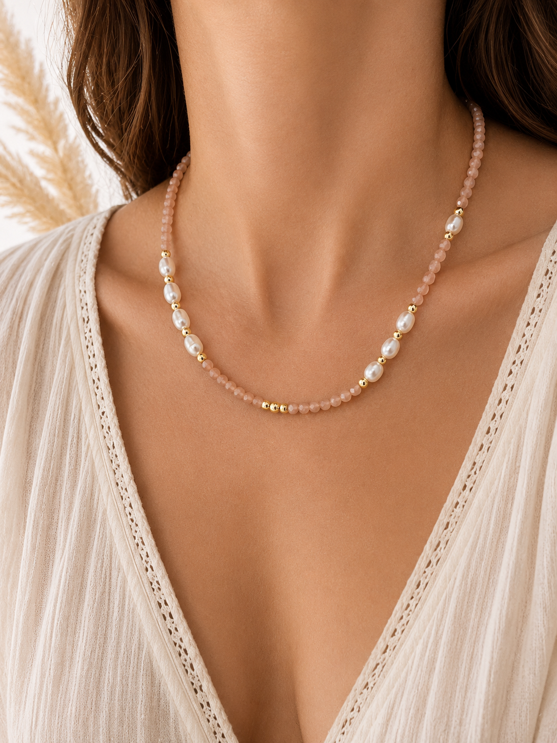 A close-up of a model wearing a delicate necklace made of pale sunstone beads, white pearls, and small gold spacer beads, paired with a cream-colored lace-trimmed top.