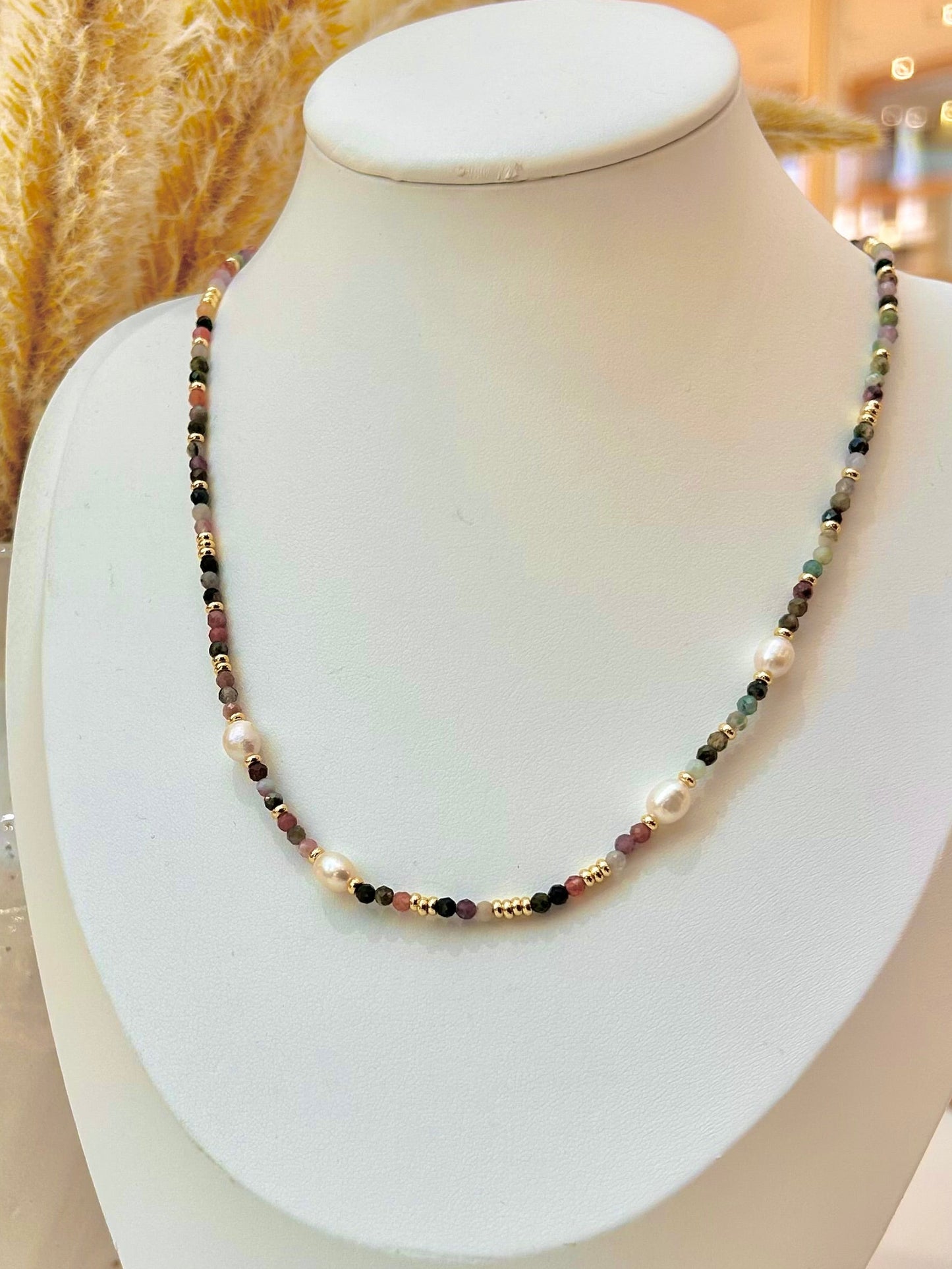 
                  
                    A beaded necklace with white pearls, gold spacers, and mixed sunstone gemstone beads displayed on a white mannequin bust
                  
                