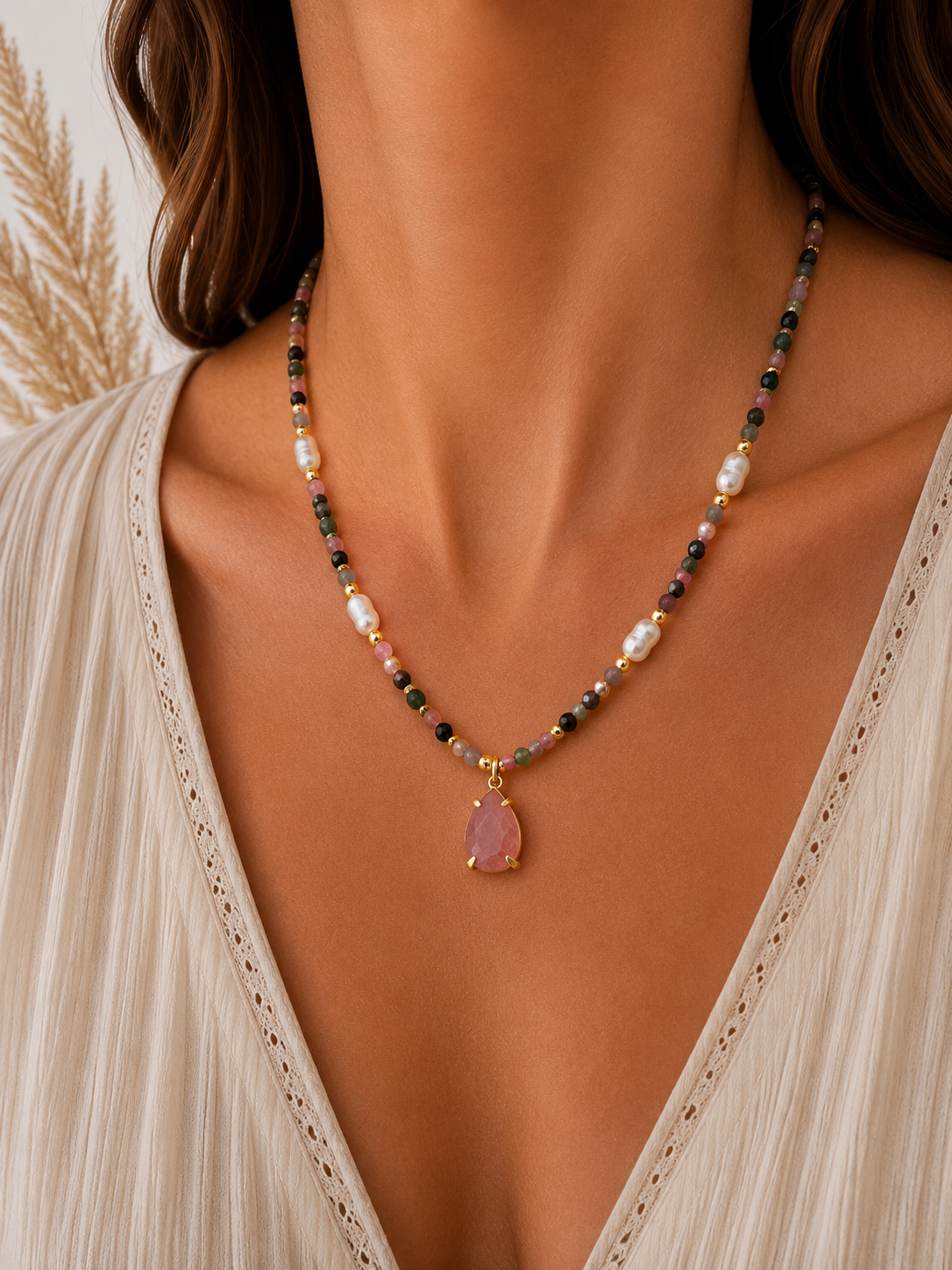 
                  
                    A close-up of a woman wearing a delicate beaded necklace with a sunstone teardrop pendant. The necklace features small  mixed sunstone beads, white freshwater pearl beads, and gold-toned metal accents.
                  
                