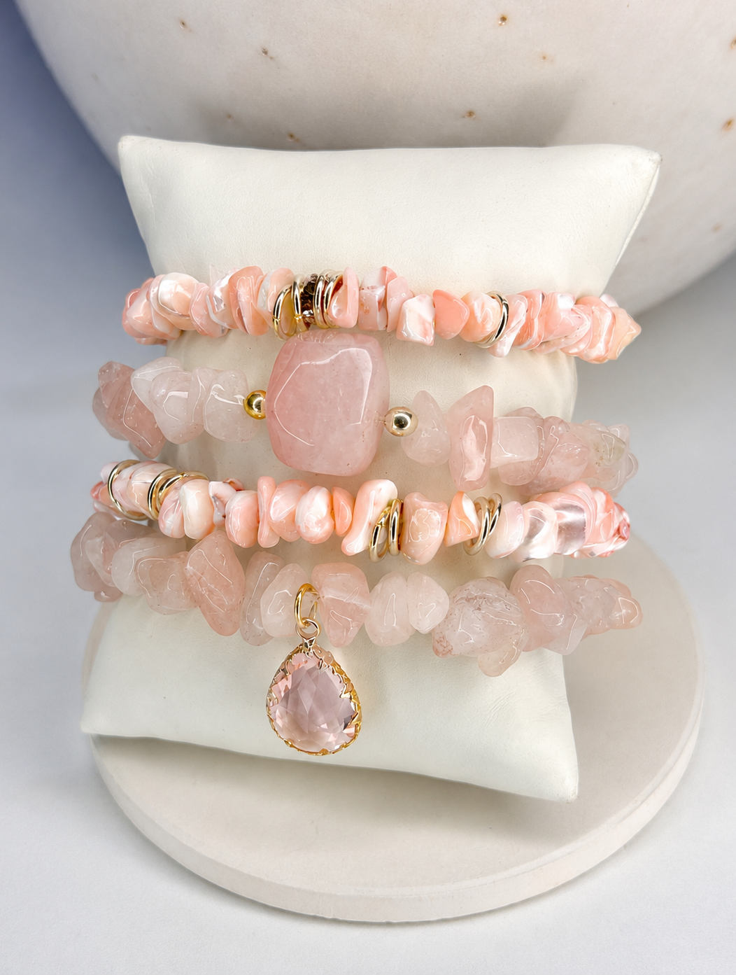 Stack of pink rose quartz mix stone bracelets on a white stand with a marble background
