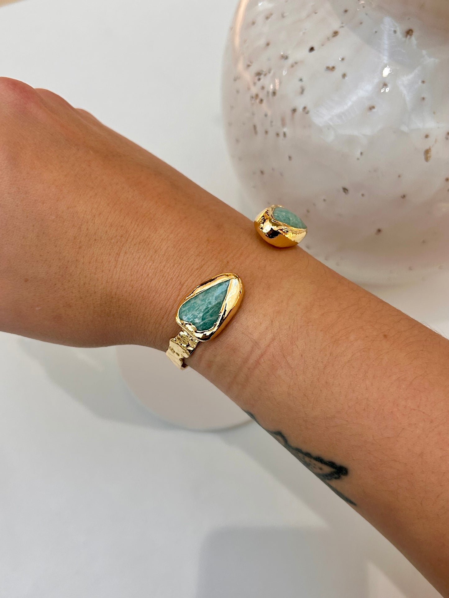 A gold-plated double cuff bracelet with a teardrop-shaped amazonite stone, shown worn on a person's wrist.