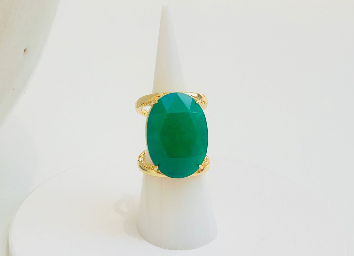
                  
                    A gold ring with a large oval-cut green jade gemstone, displayed on a white cone ring stand against a clean white background.
                  
                