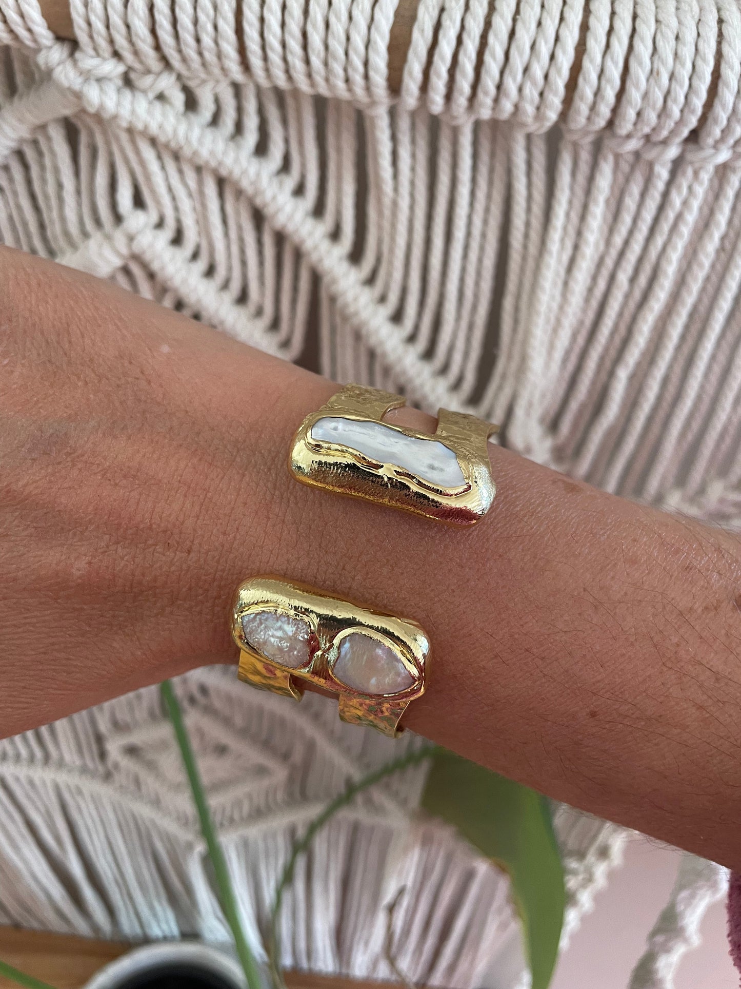 
                  
                    Gold double bangle with freshwater pearl on a wrist against a textured beige background
                  
                