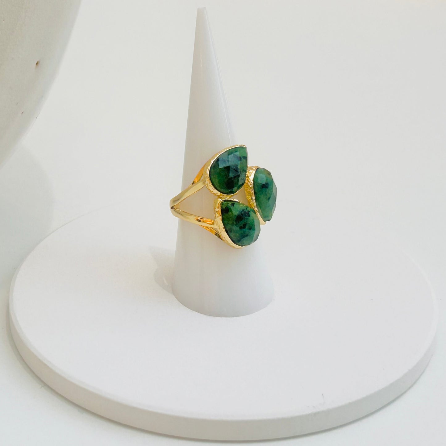 
                  
                    A gold ring with three green marquise-cut african turquoise gemstones, displayed on a white cone stand against a white background.
                  
                