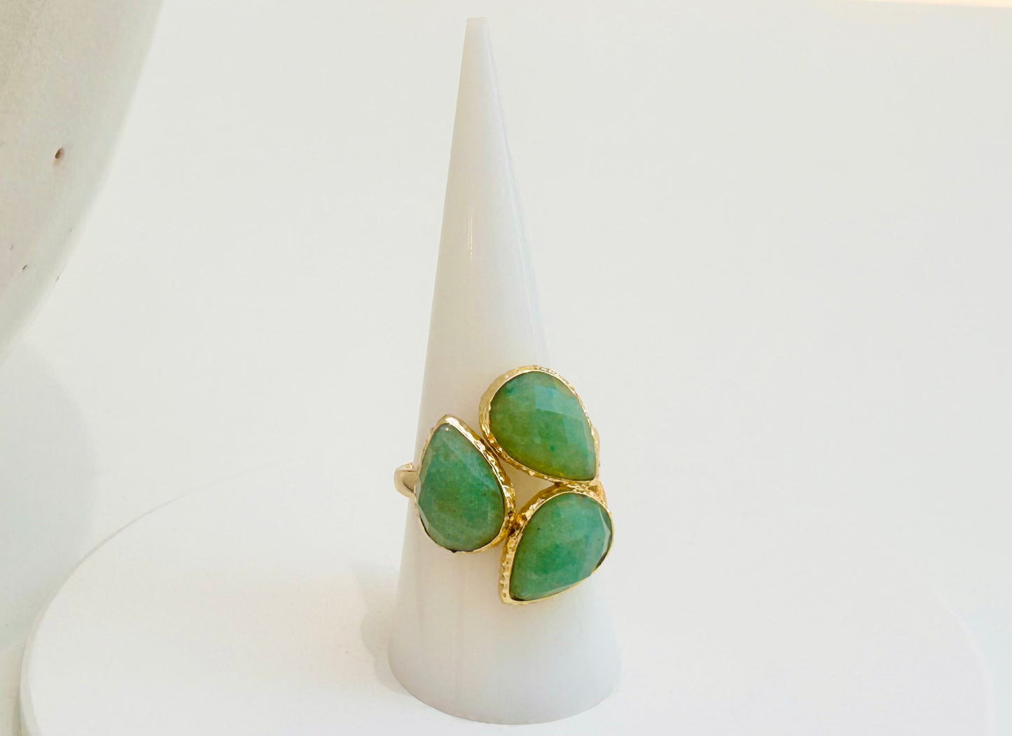 
                  
                    A gold ring with three green teardrop-shaped green Aventurine gemstones, displayed on a white cone stand against a white background.
                  
                